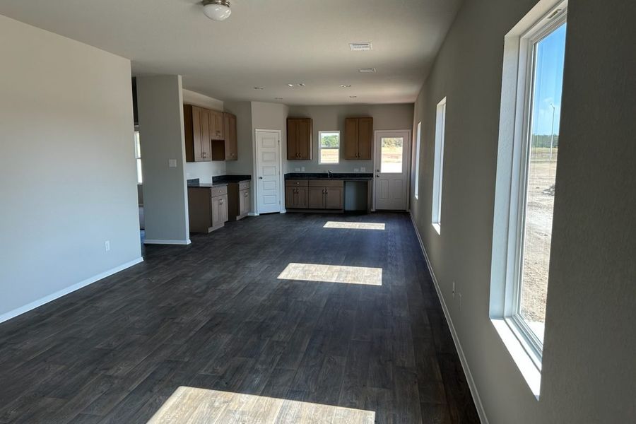 Image of home living areas with kitchen in rear. Wood-look flooring, white walls and windows down one wall, on rear door, and over sink. Image of home living areas with kitchen in rear. Wood-look flooring, white walls and windows down one wall, on rear door, and over sink.