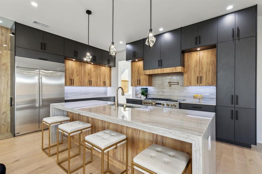 Kitchen with built in fridge, a breakfast bar, decorative light fixtures, sink, and a center island with sink