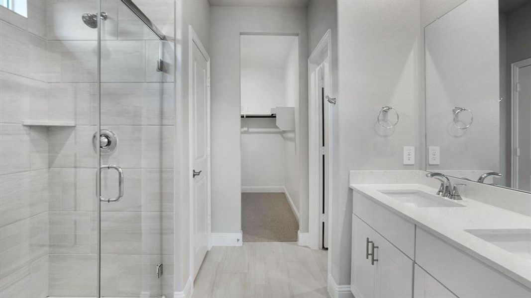 Bathroom with a walk in closet, double vanity, and a stall shower