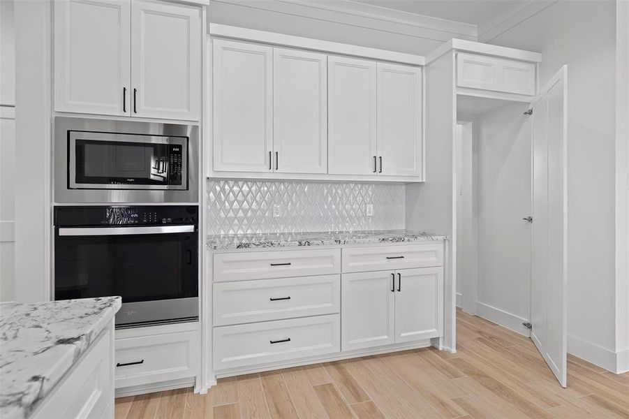 Kitchen with backsplash, ornamental molding, white cabinets, appliances with stainless steel finishes, and light hardwood / wood-style floors