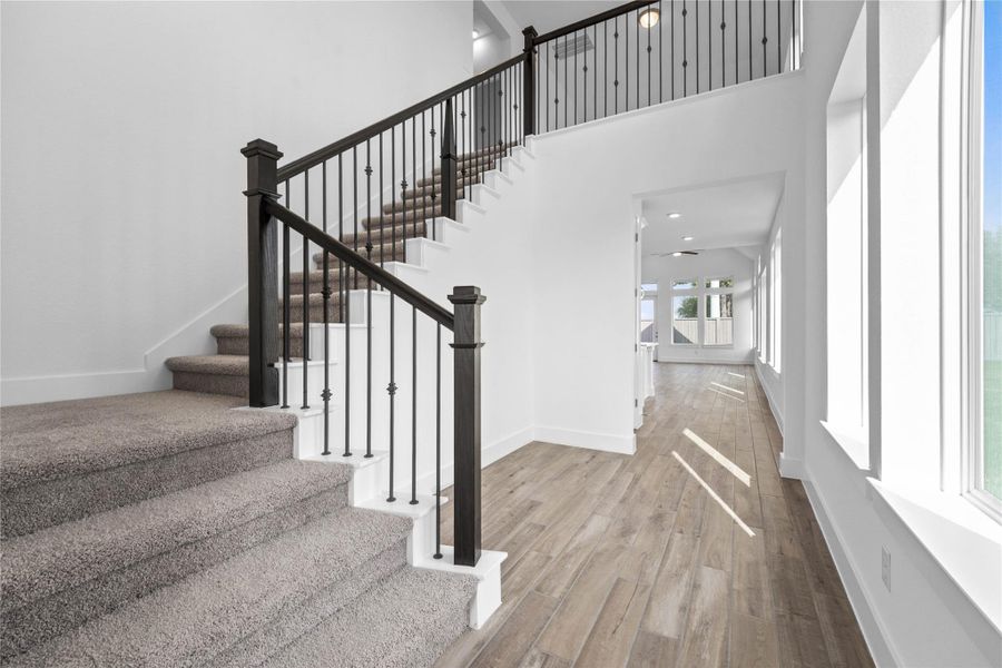 A striking, modern open staircase that creates a grand focal point in the home's entryway. It features a contemporary design with black iron balusters and elegant, dark-stained wood newel posts and handrails.