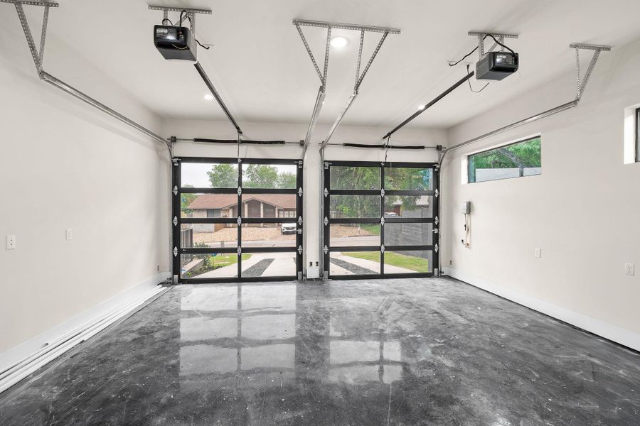 Two-car garage featuring full-view glass garage doors, polished concrete flooring, recessed lighting, and high ceilings with automatic openers