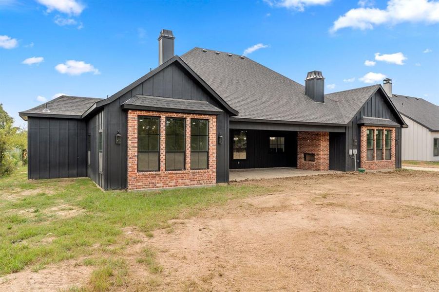 Rear view of house featuring a chimney, board and batten siding, roof with shingles, and a patio
