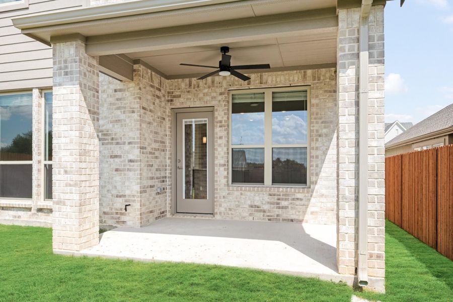 Covered back patio with ceiling fan, brick exterior, glass door, and concrete floor overlooking green lawn