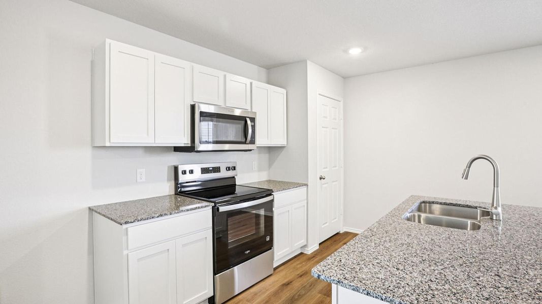 Kitchen featuring white shaker cabinetry, stainless steel appliances, granite-style countertops, wood-finish flooring, and a stainless steel double basin sink with a gooseneck faucet