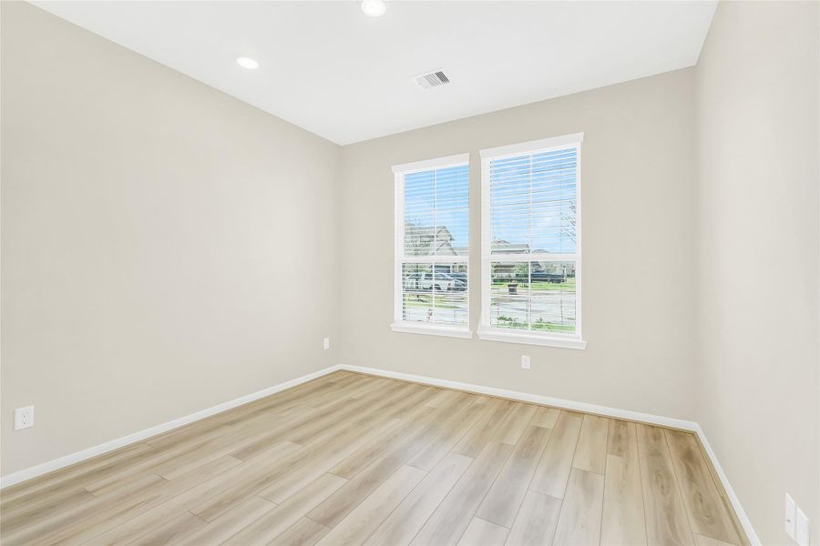 Bright secondary bedroom with large windows, high ceilings, and warm wood-tone flooring—offering a versatile space ideal for a bedroom, office, or flex room.
