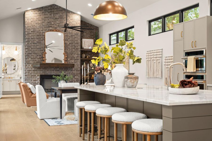Kitchen with a fireplace, lofted ceiling, light stone countertops, decorative light fixtures, and a breakfast bar