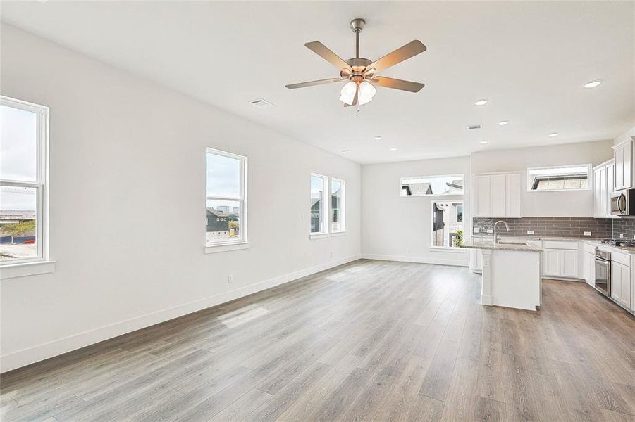 Kitchen featuring stainless steel appliances, a healthy amount of sunlight, a center island with sink, and light wood-type flooring