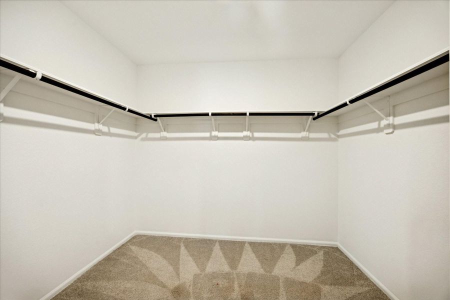 The walk-in closet with neutral carpeting and ample hanging space on both sides, perfect for organizing clothes and accessories.