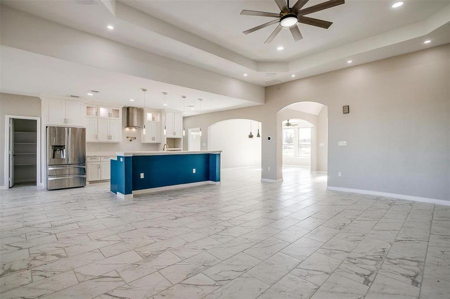 Kitchen with ceiling fan, decorative light fixtures, stainless steel fridge with ice dispenser, a center island, and white cabinetry