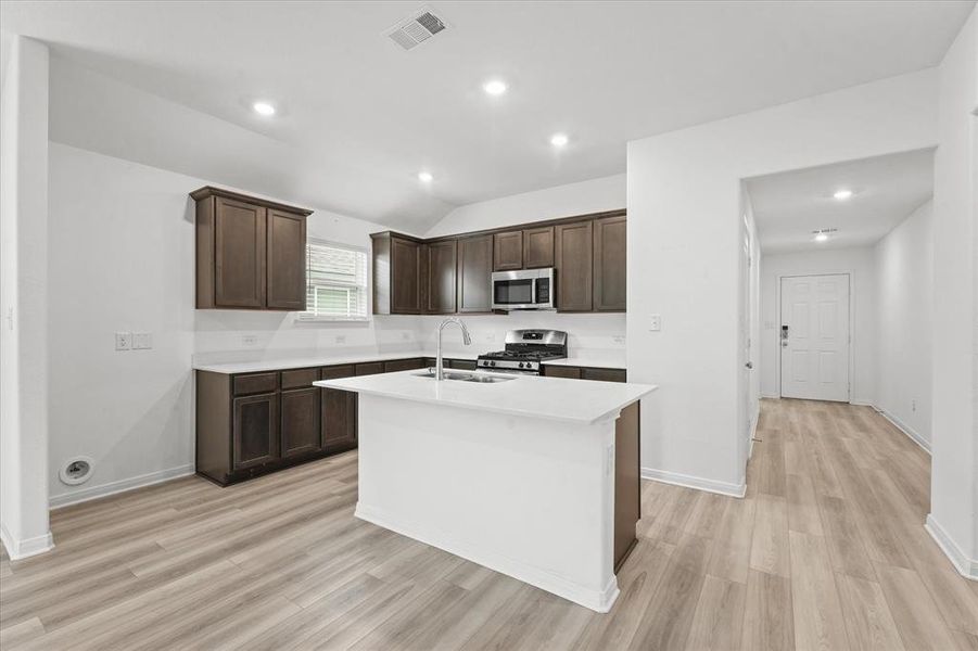 Kitchen featuring lofted ceiling, light hardwood / wood-style flooring, stainless steel appliances, and a center island with sink