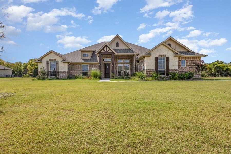View of front of property with a front yard, stone siding, a shingled roof, and brick siding View of front of property with a front yard, stone siding, a shingled roof, and brick siding