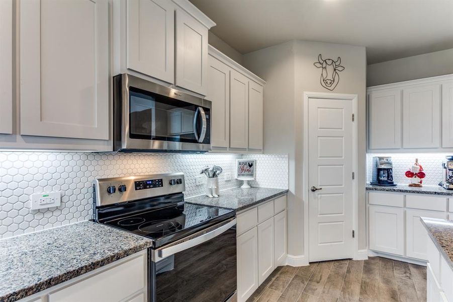 Kitchen with white cabinetry, light stone counters, light hardwood / wood-style flooring, and appliances with stainless steel finishes