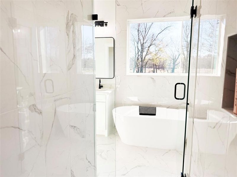 Full bathroom featuring a soaking tub, vanity, a marble finish shower, and stone wall
