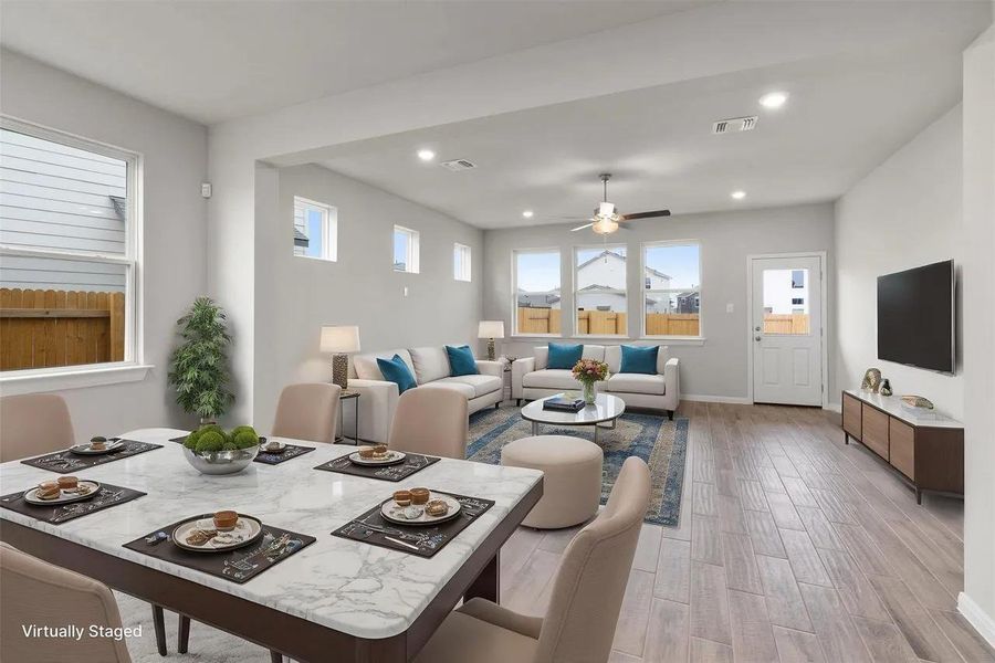 An open floorplan seamlessly connects the dining area with a naturally illuminated living space, featuring recessed lighting and a ceiling fan.