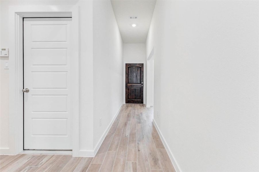 Step into a bright, elongated entry hallway featuring wood-look tile flooring and crisp white walls. The warm contrast of the solid wood front door at the far end provides a luxurious focal point, setting the tone for the home's clean, modern design throughout. Step into a bright, elongated entry hallway featuring wood-look tile flooring and crisp white walls. The warm contrast of the solid wood front door at the far end provides a luxurious focal point, setting the tone for the home's clean, modern design throughout.