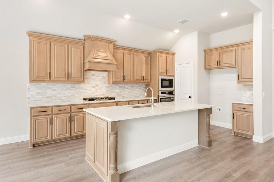 Kitchen with light wood cabinets, center island with sink, tile backsplash, and stainless steel appliances on wood-look floors Kitchen with light wood cabinets, center island with sink, tile backsplash, and stainless steel appliances on wood-look floors