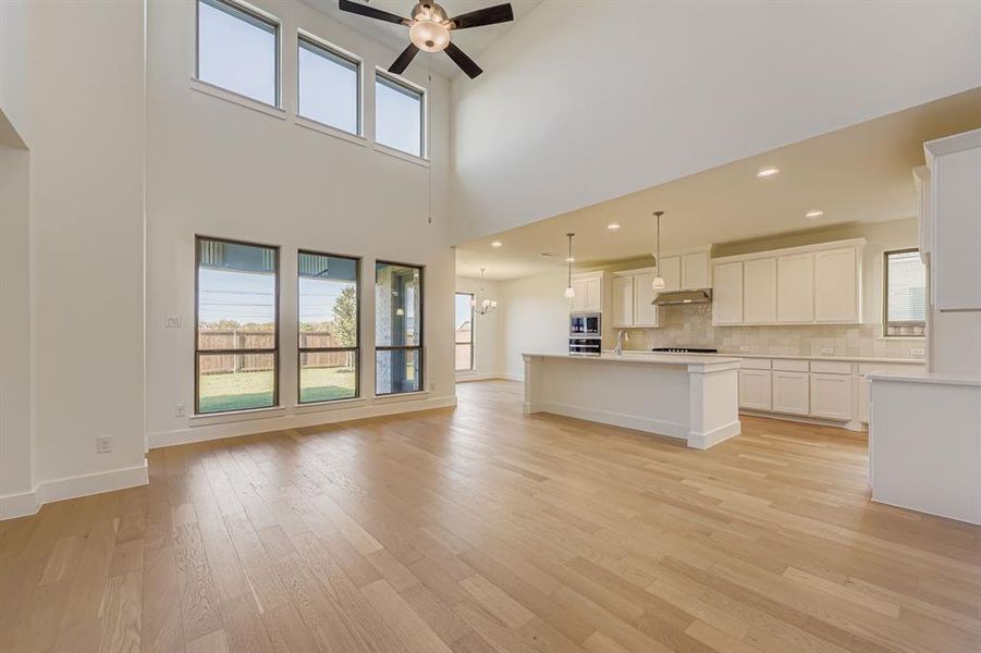 Unfurnished living room featuring light wood-style flooring, a ceiling fan, a chandelier, a towering ceiling, and recessed lighting Unfurnished living room featuring light wood-style flooring, a ceiling fan, a chandelier, a towering ceiling, and recessed lighting
