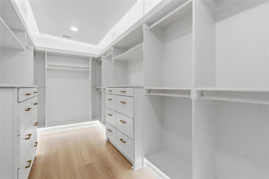 Custom-designed walk-in closet featuring extensive built-in shelving, multiple hanging rods, integrated drawer units with brass-finish hardware, recessed ceiling lighting, and perimeter floor lighting Custom-designed walk-in closet featuring extensive built-in shelving, multiple hanging rods, integrated drawer units with brass-finish hardware, recessed ceiling lighting, and perimeter floor lighting