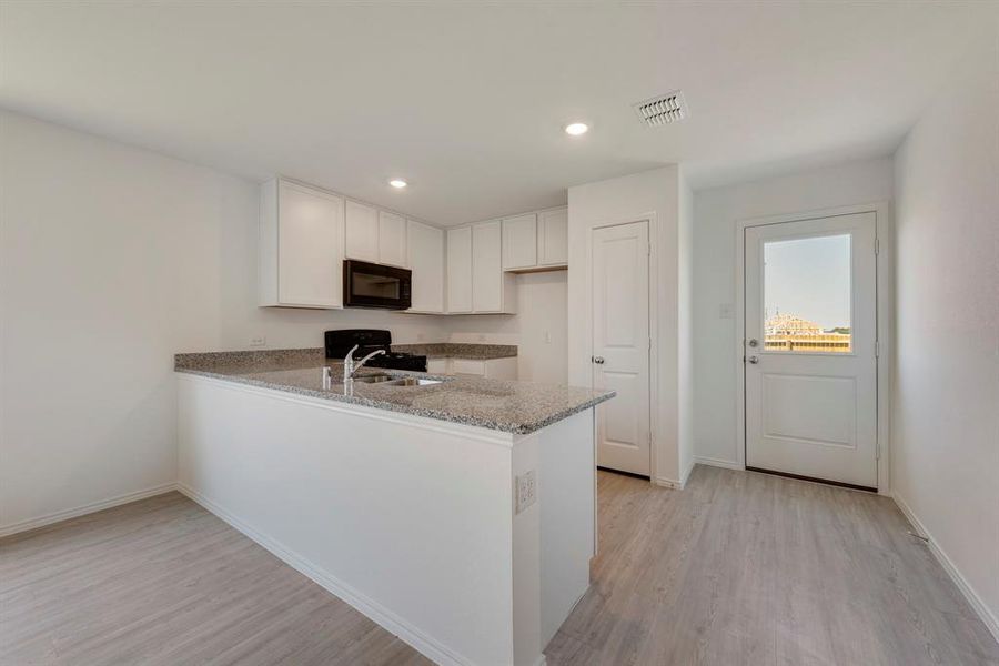 Kitchen featuring light hardwood / wood-style floors, kitchen peninsula, light stone counters, and white cabinets