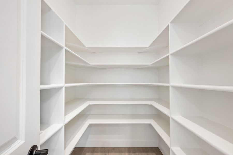 Walk-in pantry with white wrap-around shelving on three walls and hardwood floors
