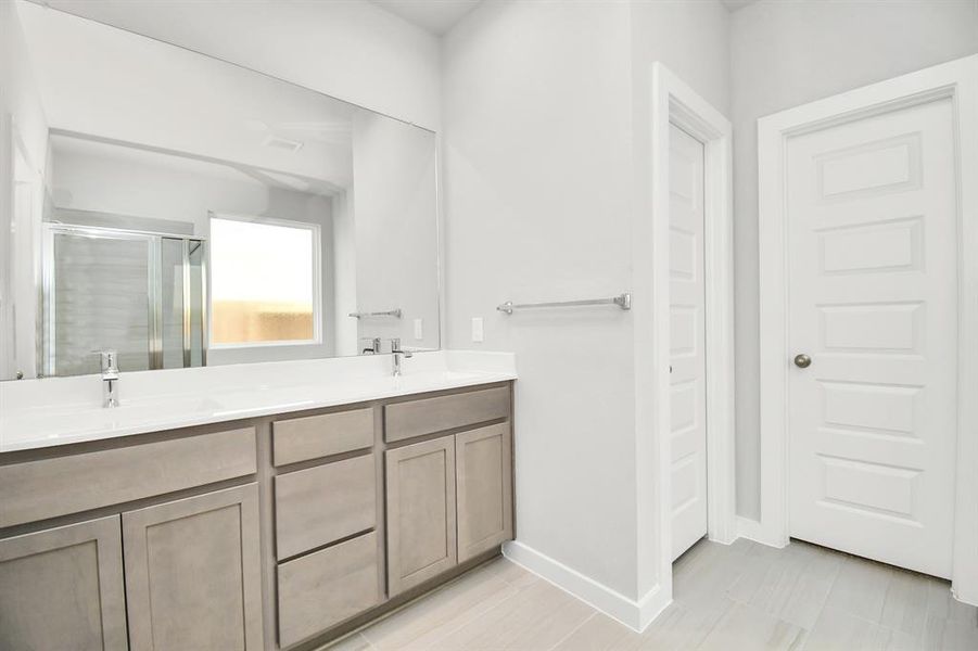 The sophisticated vanity, featuring double sinks, dark-colored countertops, contemporary hardware, and bright recessed lighting, adds both style and functionality to the space. Example photo of completed home with similar plan. Actual may vary.