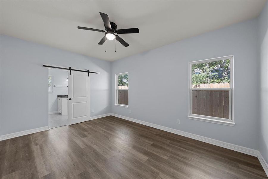 Unfurnished bedroom featuring a barn door, wood finished floors, ceiling fan, and ensuite bath