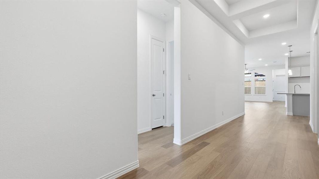 Hallway featuring wood-finish flooring, crisp white walls, recessed lighting, and a coffered ceiling detail Hallway featuring wood-finish flooring, crisp white walls, recessed lighting, and a coffered ceiling detail
