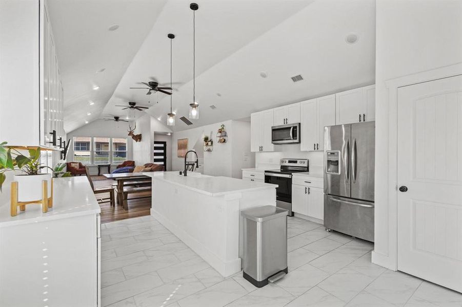 Kitchen featuring open floor plan, white cabinetry, appliances with stainless steel finishes, lofted ceiling, and light marble finish flooring