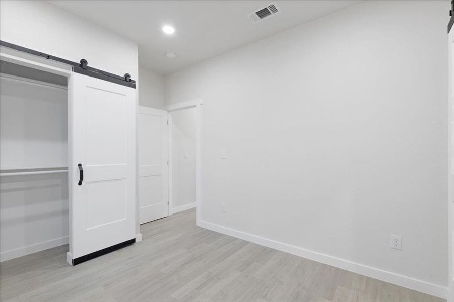 Unfurnished bedroom featuring a barn door, light hardwood / wood-style floors, and a closet