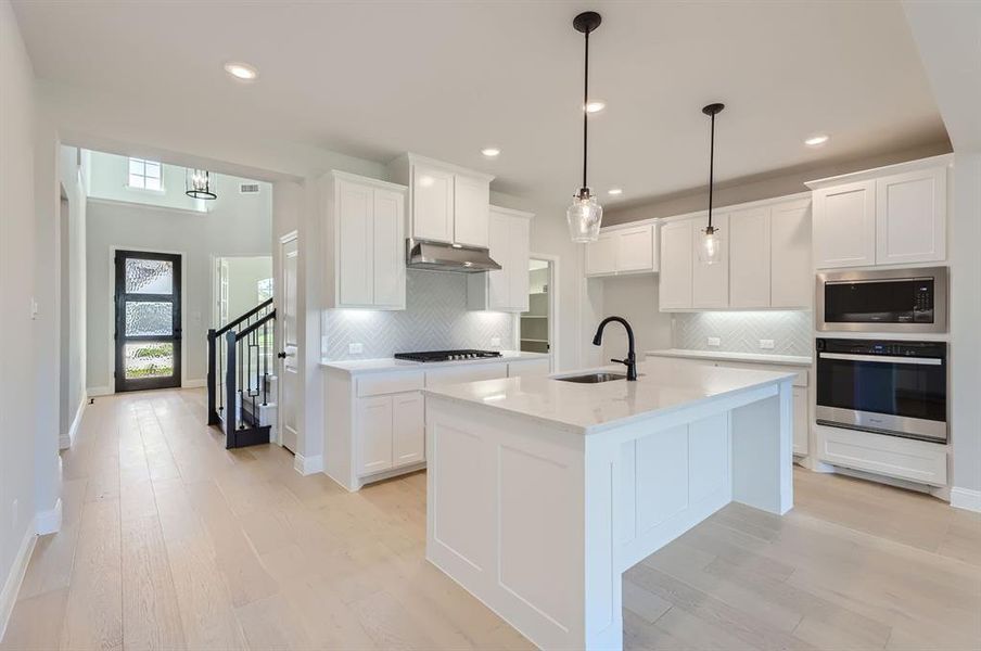 Kitchen featuring appliances with stainless steel finishes, a center island with sink, sink, and white cabinets