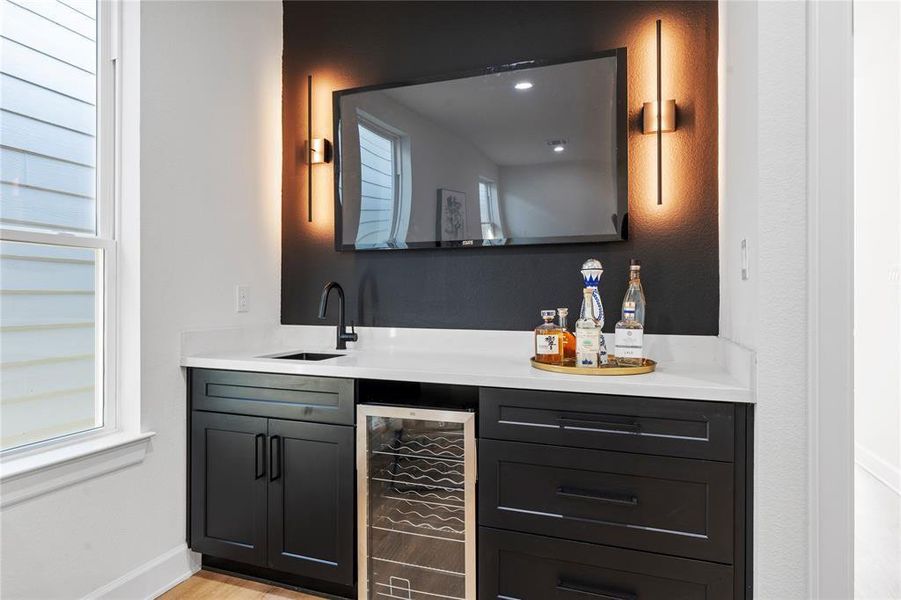Elegant wet bar featuring sleek black cabinetry, a modern sink, and a wine cooler, complemented by ambient lighting and a mounted TV for a luxurious entertainment experience. Elegant wet bar featuring sleek black cabinetry, a modern sink, and a wine cooler, complemented by ambient lighting and a mounted TV for a luxurious entertainment experience.