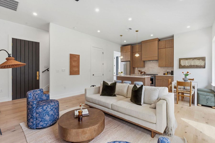 Open-concept living space featuring light wood-finish flooring, recessed lighting, and a contemporary kitchen