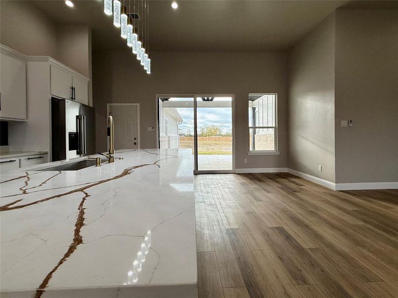 Kitchen featuring light stone counters, light wood-style flooring, white cabinetry, high quality fridge, and hanging light fixtures