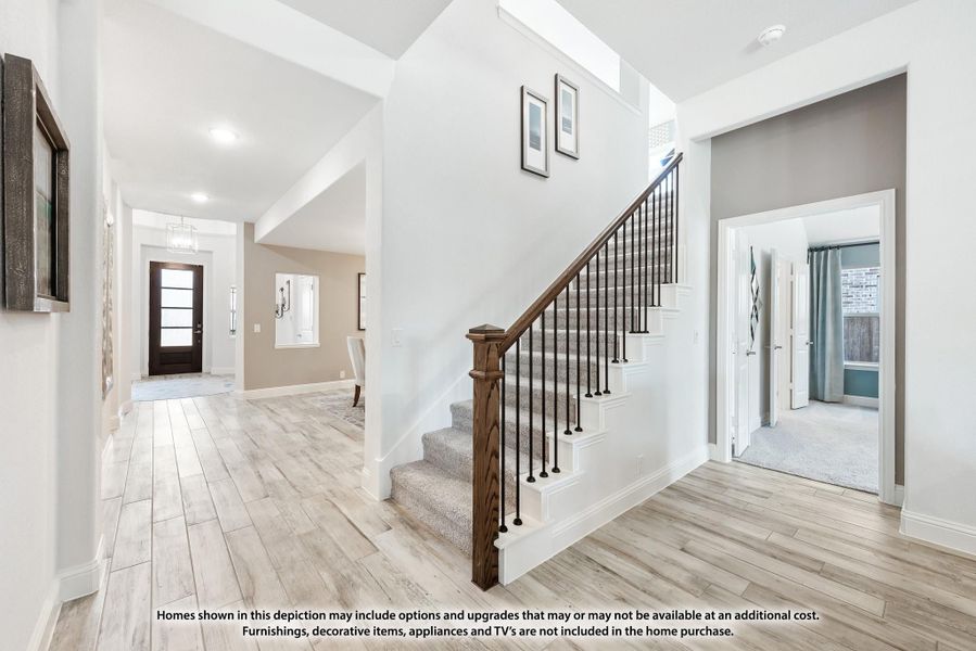 Bright home entryway with wood staircase, iron balusters, light hardwood floors, and front door view down hallway. Bright home entryway with wood staircase, iron balusters, light hardwood floors, and front door view down hallway.