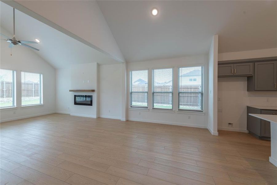 Unfurnished living room with lofted ceiling, a ceiling fan, a glass covered fireplace, baseboards, and light wood finished floors