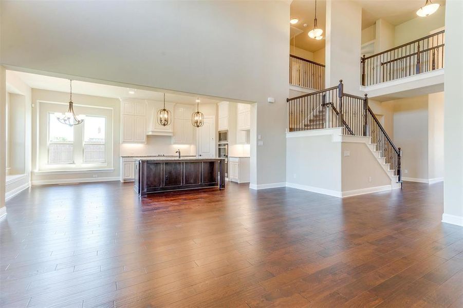 Unfurnished living room featuring a towering ceiling, an inviting chandelier, and dark hardwood / wood-style flooring