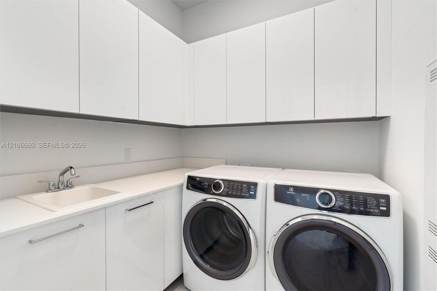 Laundry area featuring high-gloss white upper and lower cabinetry, solid surface countertop, and an integrated basin with a chrome faucet