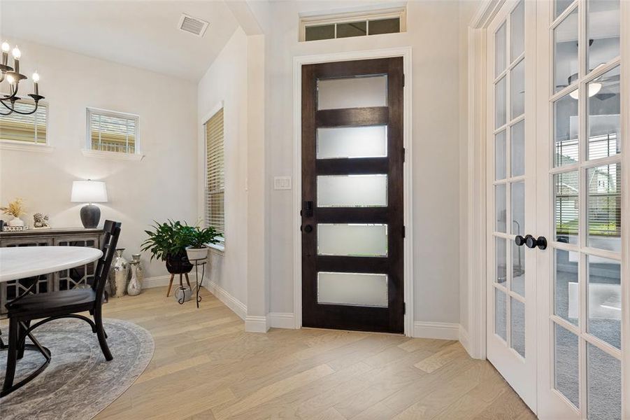 Entryway featuring a dark wood door with frosted glass panels, wood-finish flooring, white French doors, and transom windows