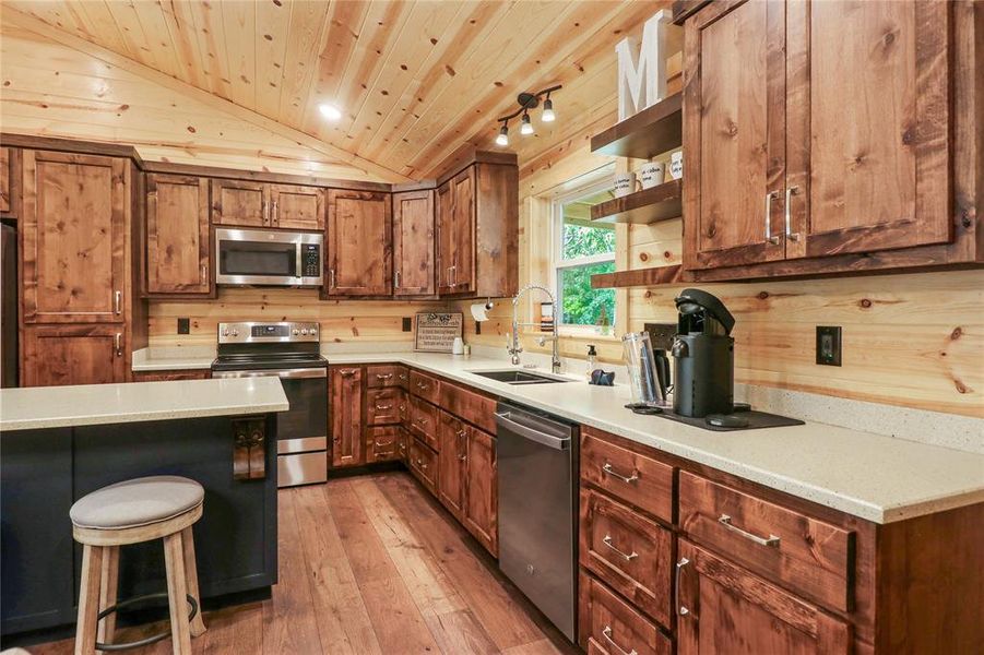 Kitchen featuring light hardwood / wood-style floors, lofted ceiling, stainless steel appliances, wooden ceiling, and sink