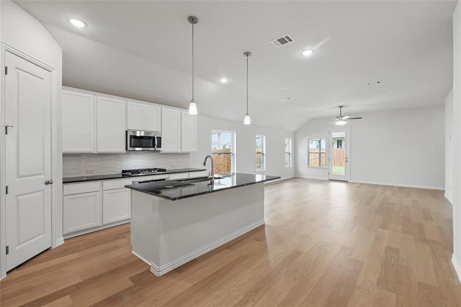 Kitchen with vaulted ceiling, white cabinetry, a center island with sink, light wood finished floors, and backsplash