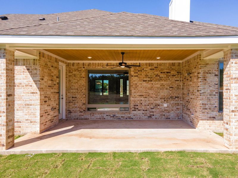 Entrance to property with a ceiling fan, a patio, roof with shingles, and brick siding