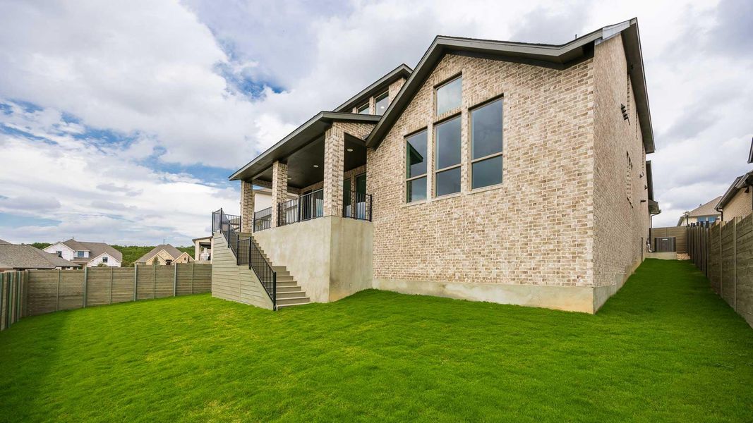 Rear view of property featuring stairs, a fenced backyard, brick siding, and a balcony