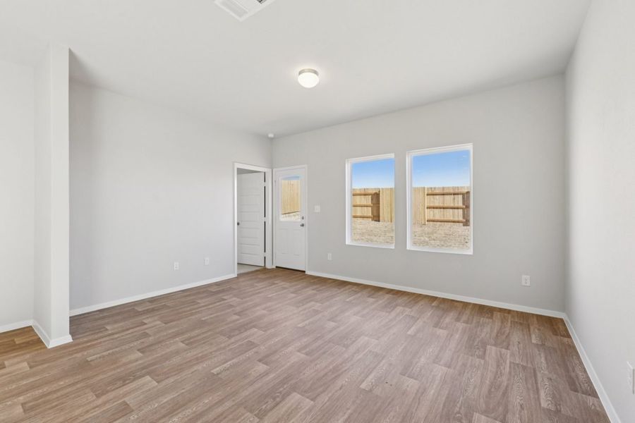 Image of a dining room with light grey walls, brown wood-look vinyl flooring, two windows and a white back door