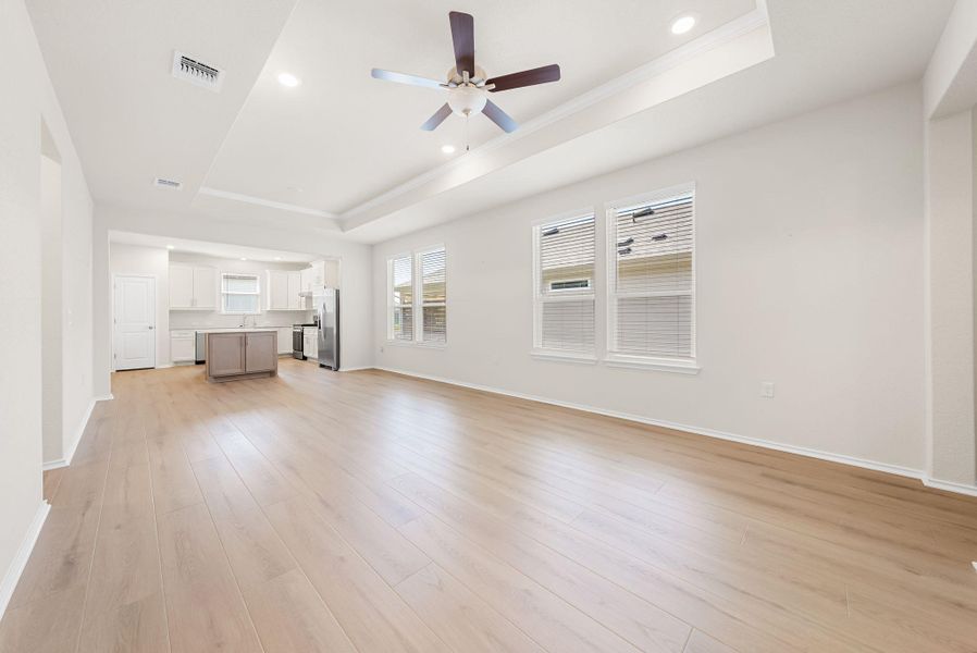 A generous open-concept living area boasts light wood flooring, a tray ceiling, and ample natural illumination. A generous open-concept living area boasts light wood flooring, a tray ceiling, and ample natural illumination.