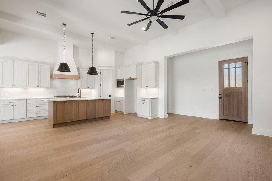 Open concept kitchen and living area featuring light wood flooring, a central kitchen island with a sink, white cabinetry, and a ceiling fan
