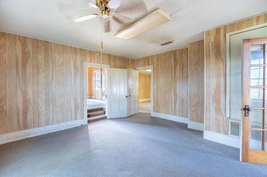 Empty room with ceiling fan, wood walls, and a textured ceiling