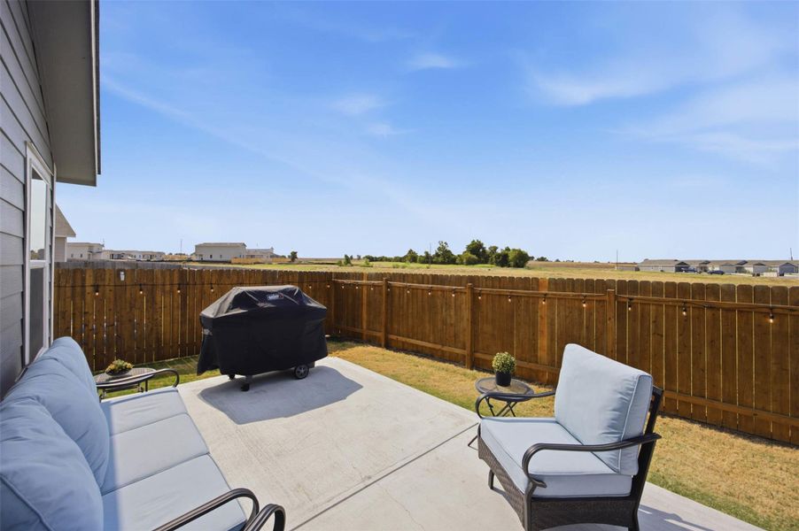 A concrete patio looks out over a fenced yard toward an open grassy horizon.