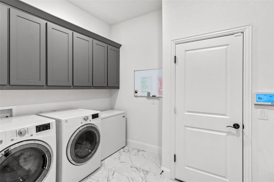 Washroom featuring light marble finish floors, washing machine and clothes dryer, and cabinet space