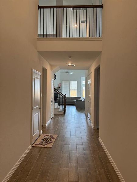 Hallway with wood-look tile flooring, white baseboards, and neutral wall tones Hallway with wood-look tile flooring, white baseboards, and neutral wall tones